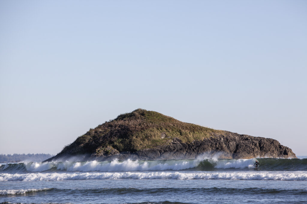 čaw̓inʔis - Lovekin Rock with surfer riding wave